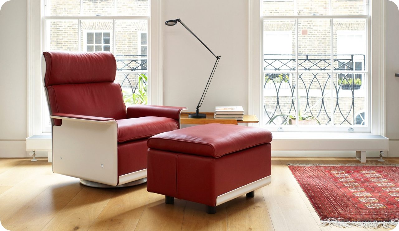 A red Dieter Rams armchair and ottoman with rounded cushions in a bright room.