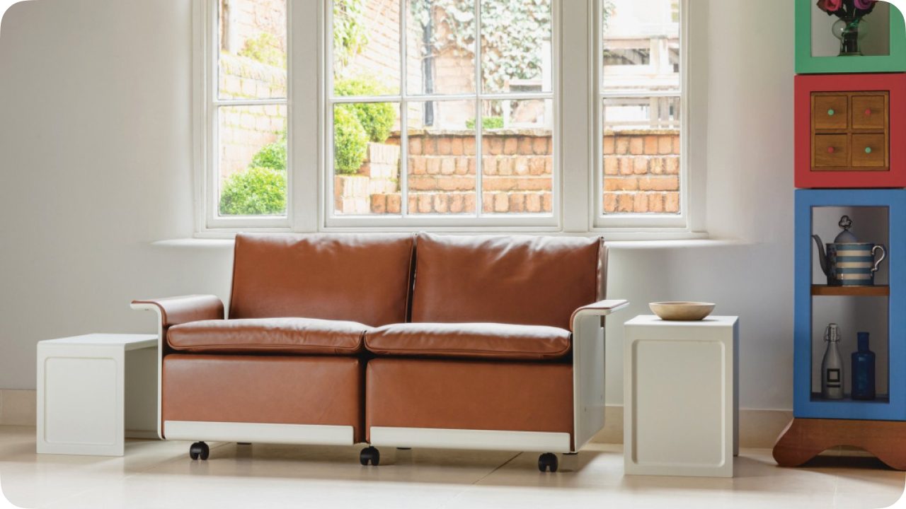 A tan leather two-seater version of the same chair, its straight-edged headrest running the full width.