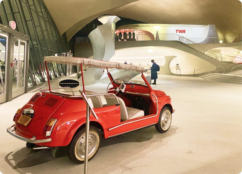 A red vintage Citroën with rounded fenders and lights, parked under the curved ceiling of the TWA Hotel.